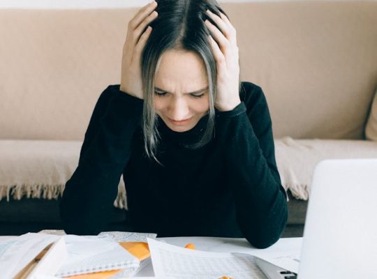 A woman appears stressed and overwhelmed with paperwork at her home desk.