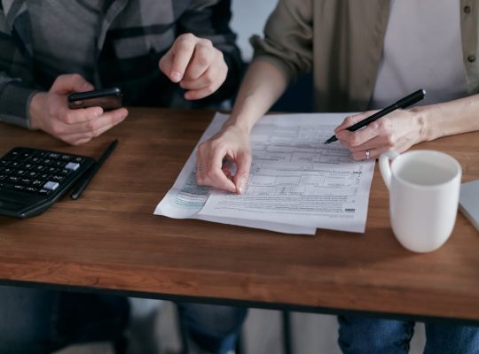 Couple managing finances at home with a calculator, smartphone, and documents.