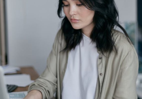 Focused young woman working on a laptop at her desk, managing finances.
